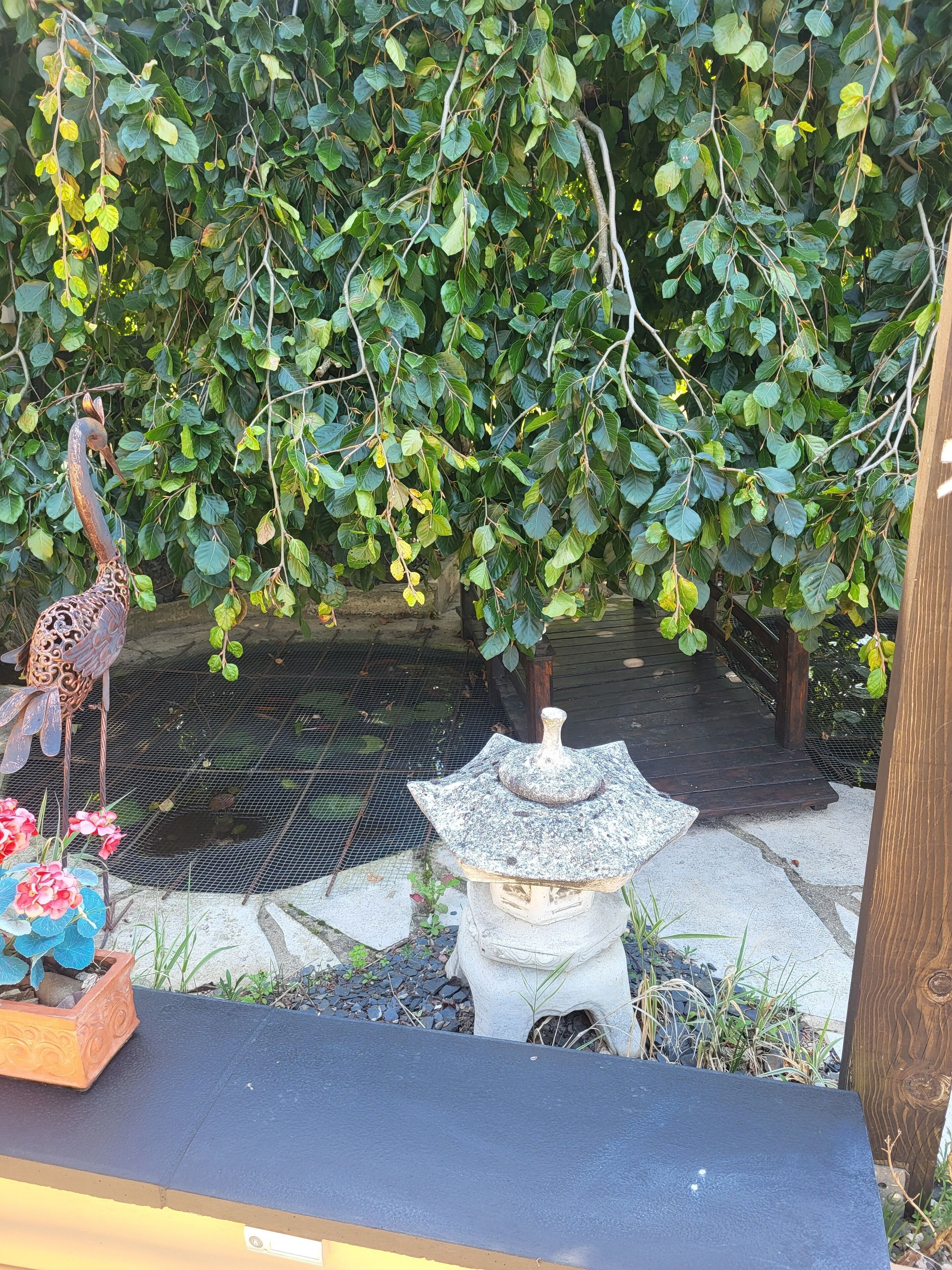 Un jardin agrémenté d’une statue d’oiseau, d’un nichoir décoratif et d’une petite table en pierre.