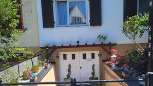 Un edificio residencial con entrada protegida por una reja, un pequeño jardín con plantas en macetas y un techo de tejas.