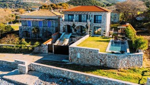 A stone villa with a swimming pool, set against a mountainous backdrop.