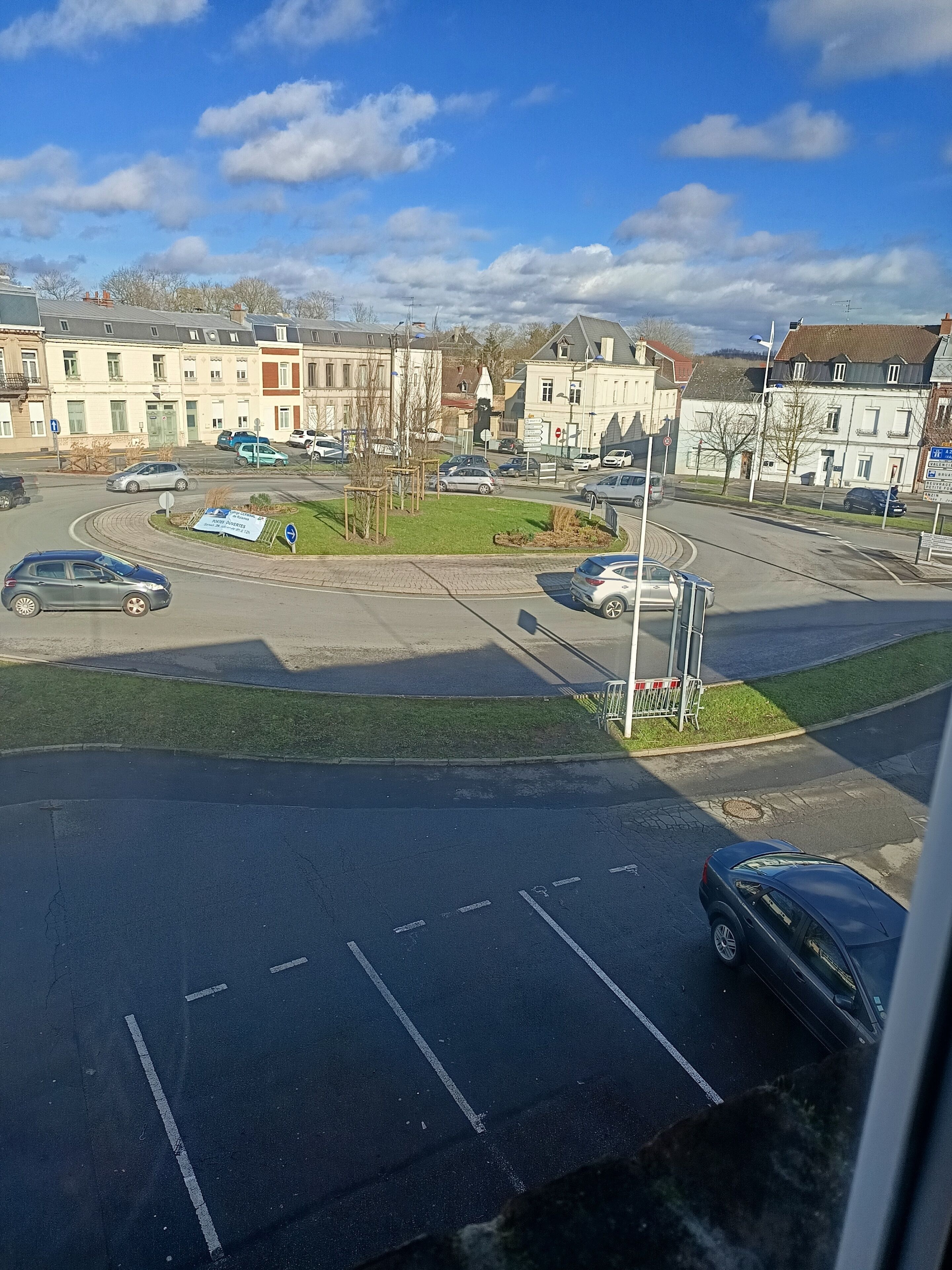 Ein Parkplatz mit mehreren Autos, einer Grünfläche und Gebäuden im Hintergrund.