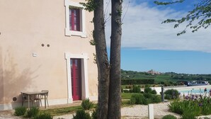Un edificio con puerta roja y ventanas, una mesa y sillas afuera, y vistas del paisaje.