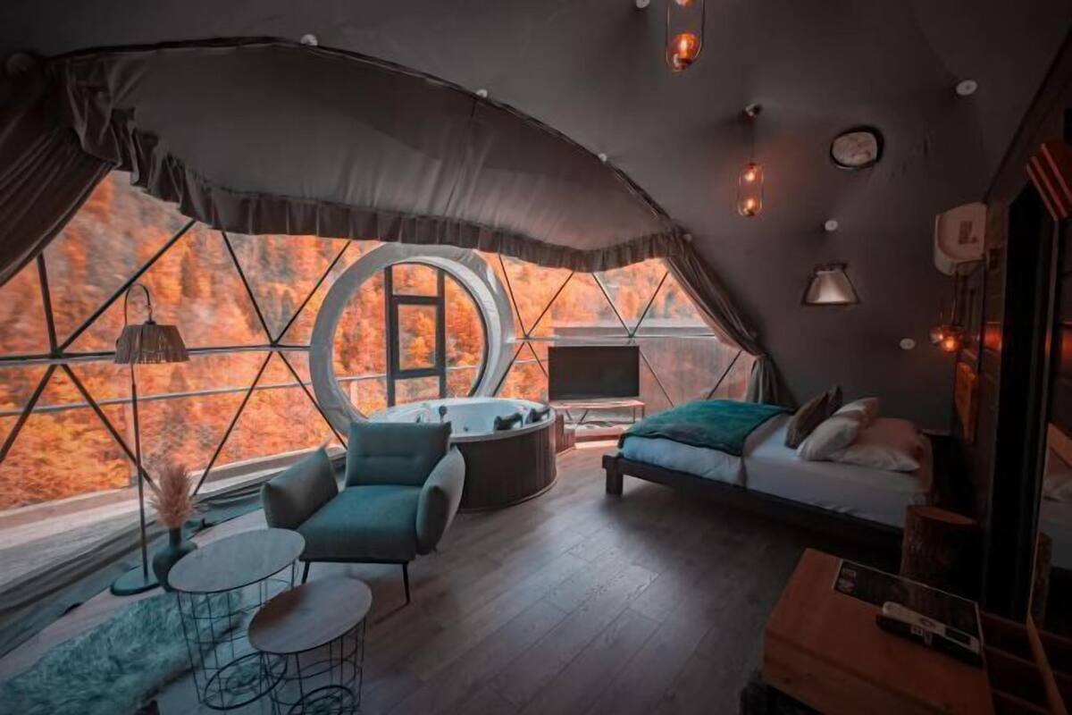 Un intérieur chaleureux avec une fenêtre ronde, un canapé, un fauteuil, une petite table et une cheminée.