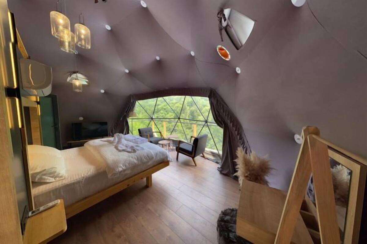 Une chambre confortable avec un lit, un bureau et une chaise, une grande fenêtre et un luminaire au plafond.