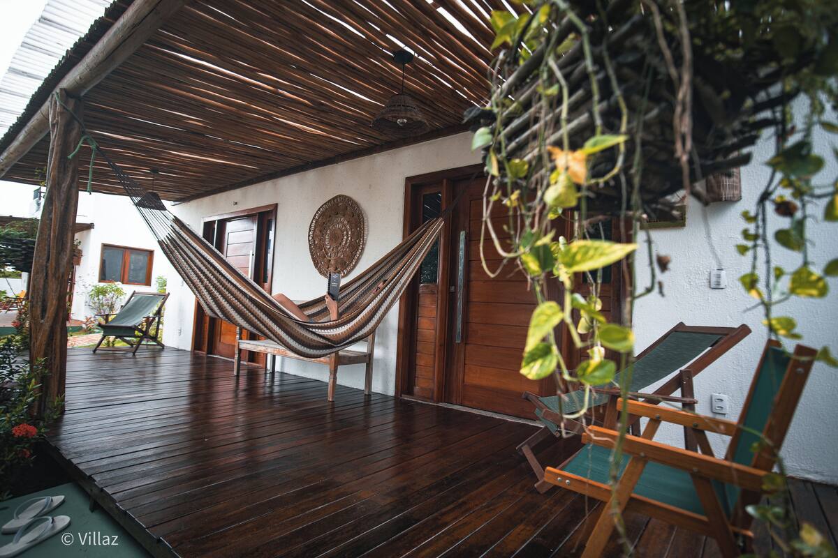Une terrasse en bois avec un hamac, deux chaises longues et un mur blanc orné d’une assiette décorative.