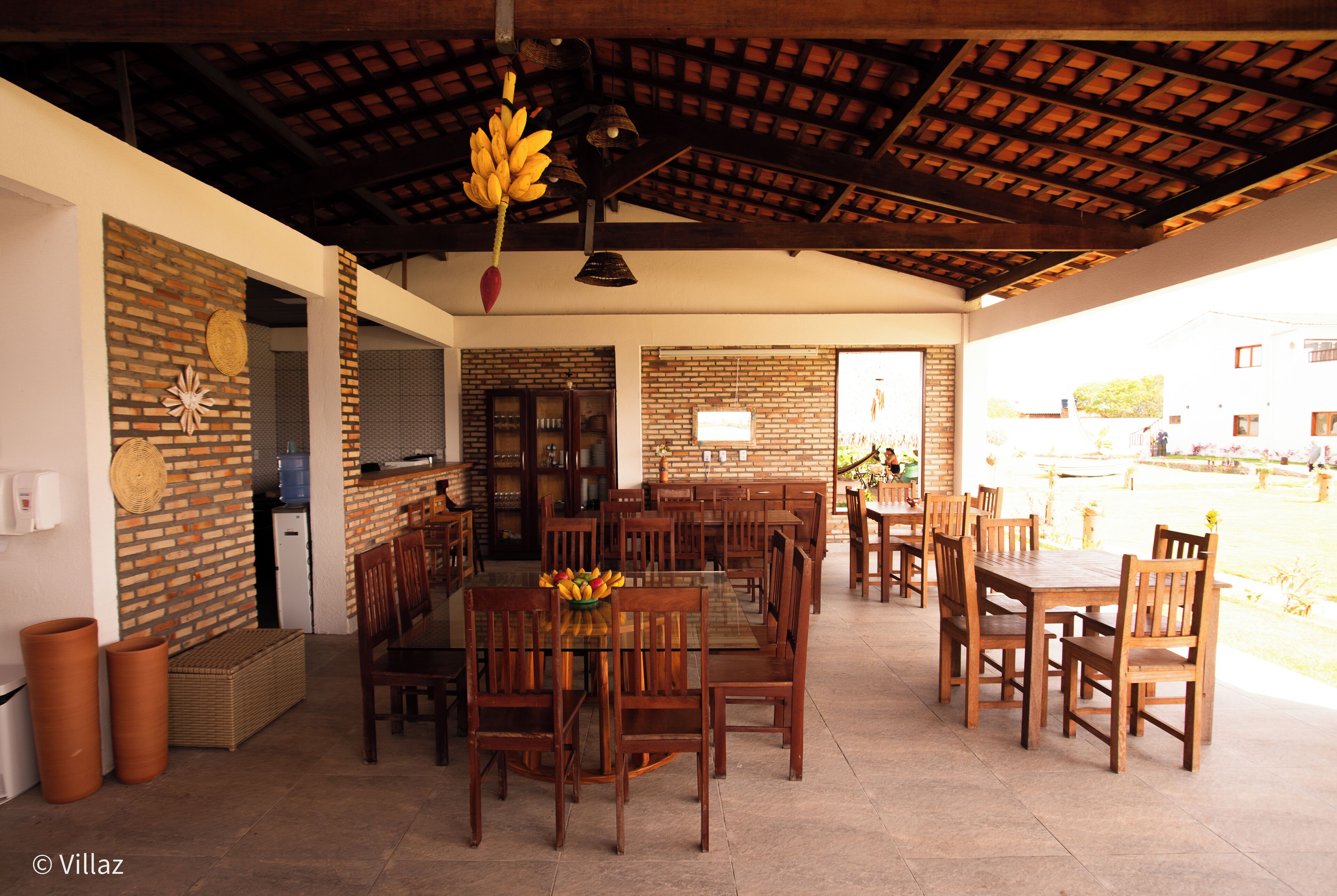 An open-plan dining area with brick walls, wooden tables and chairs, and a hanging plant.