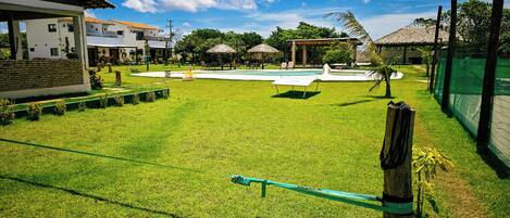 Uma área externa com gramado, piscina, cadeiras de descanso e um edifício com telhado em azulejo.