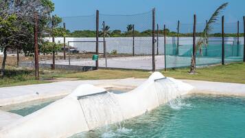 A water feature with a cascading waterfall, surrounded by a fenced area with a grassy lawn and a clear sky.