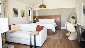 A modern hotel room with a large bed, a sofa, a desk, and a dining area. - The Compass McMinnville (McMinnville)