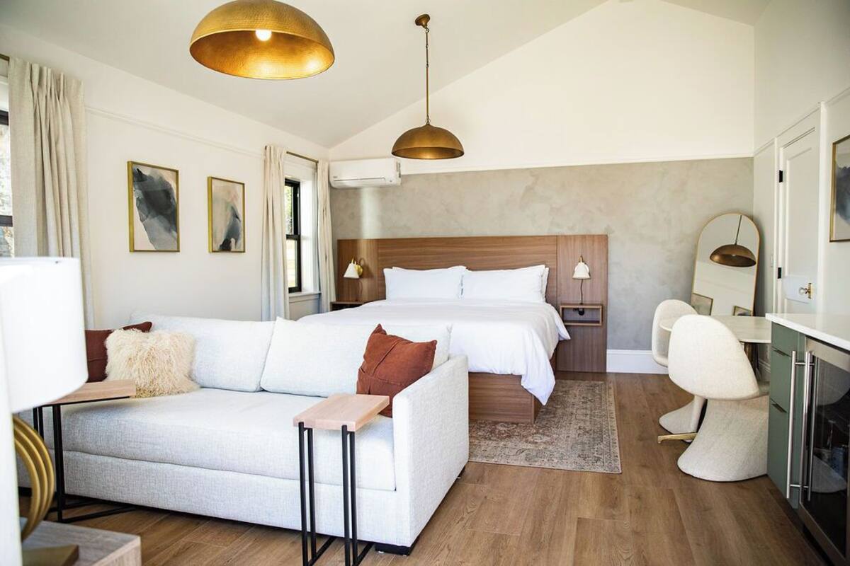 A modern hotel room with a large bed, a sofa, a desk, and a dining area.