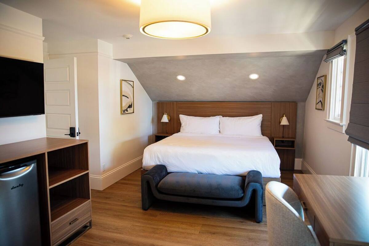 A modern hotel room with a large bed, a flat-screen TV, a wooden cabinet, and a bench.