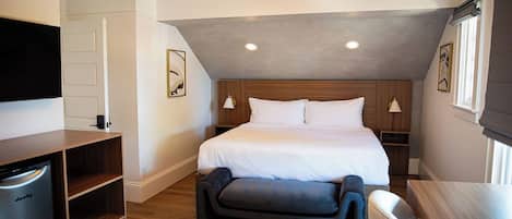 A modern hotel room with a large bed, a flat-screen TV, a wooden cabinet, and a bench.