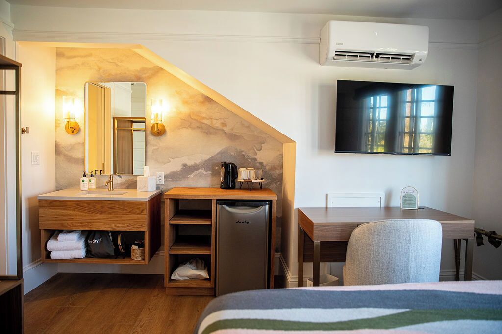 Habitación de hotel con tocador de madera, refrigerador empotrado, escritorio, silla, televisor de pantalla plana y ventana grande.