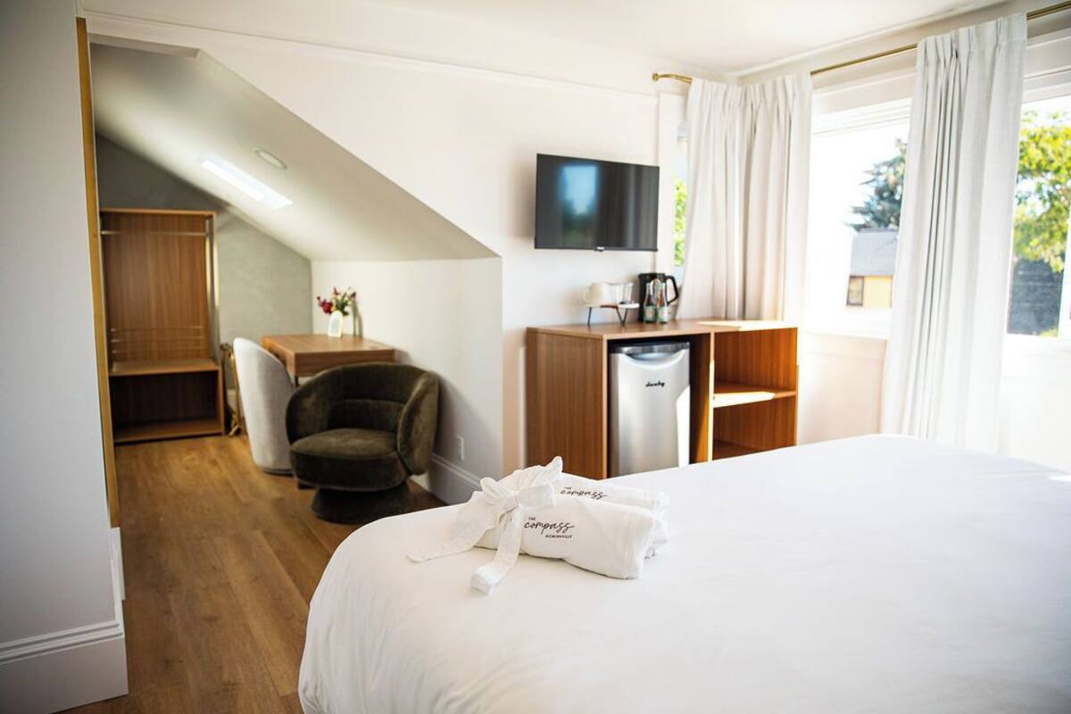A hotel room with a bed, a desk, a chair, a TV, and a window with curtains.