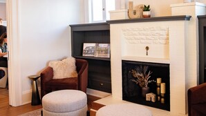 A living room with a fireplace, ottomans, a brown armchair, and a modern chandelier. - The Compass McMinnville (McMinnville)