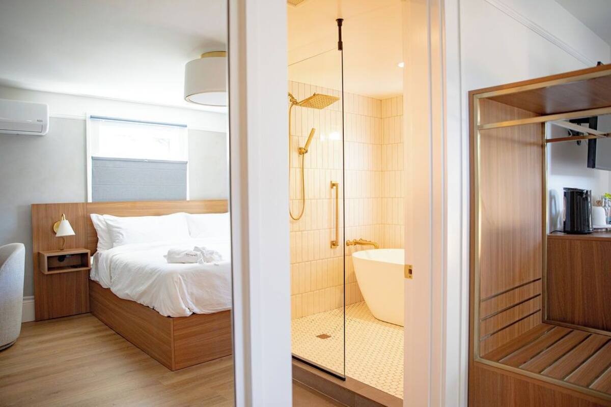 A modern hotel room with a wooden bed, a glass shower enclosure, and a walk-in closet.