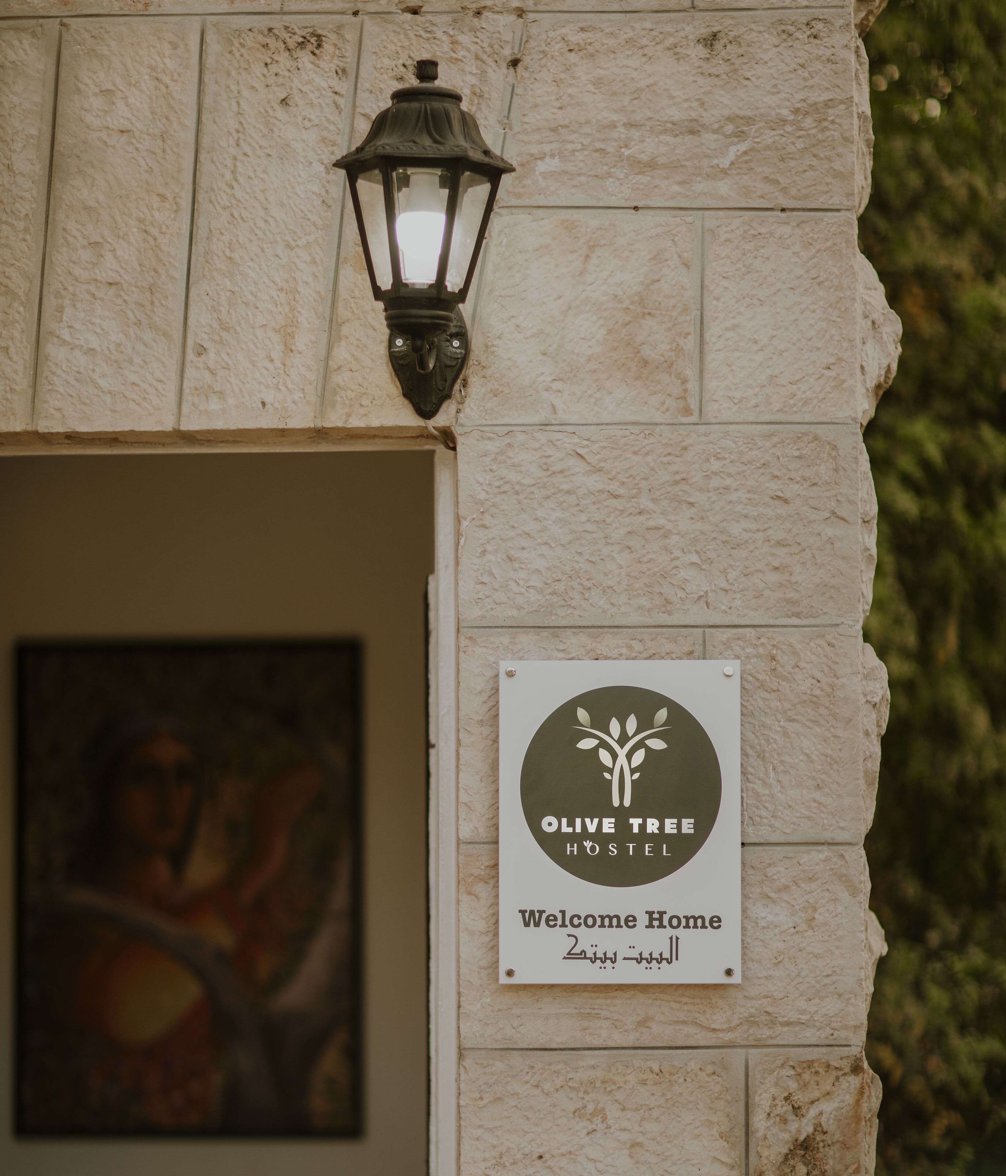 Naamplaatje voor Olive Tree Hostel met een gastvrije boodschap en een logo.