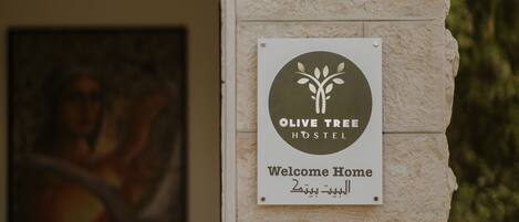Naamplaatje voor Olive Tree Hostel met een gastvrije boodschap en een logo.
