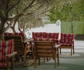 A seating area with wooden chairs and benches, some with red and white patterned cushions.
