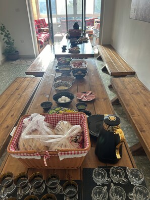 A long wooden table with various bowls and baskets containing food items, arranged for a meal. - OliveTreeHostel (Ramallah)