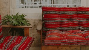 A balcony with a view of a cityscape, a wooden bench, and a red patterned sofa. - OliveTreeHostel (Ramallah)