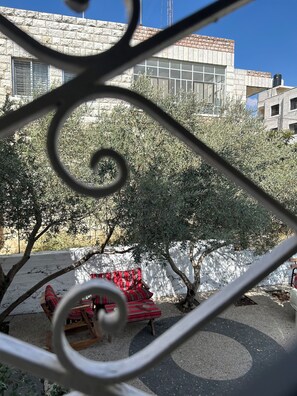 A courtyard with a red patterned sofa, a tree, and a building with stone walls and windows. - OliveTreeHostel (Ramallah)