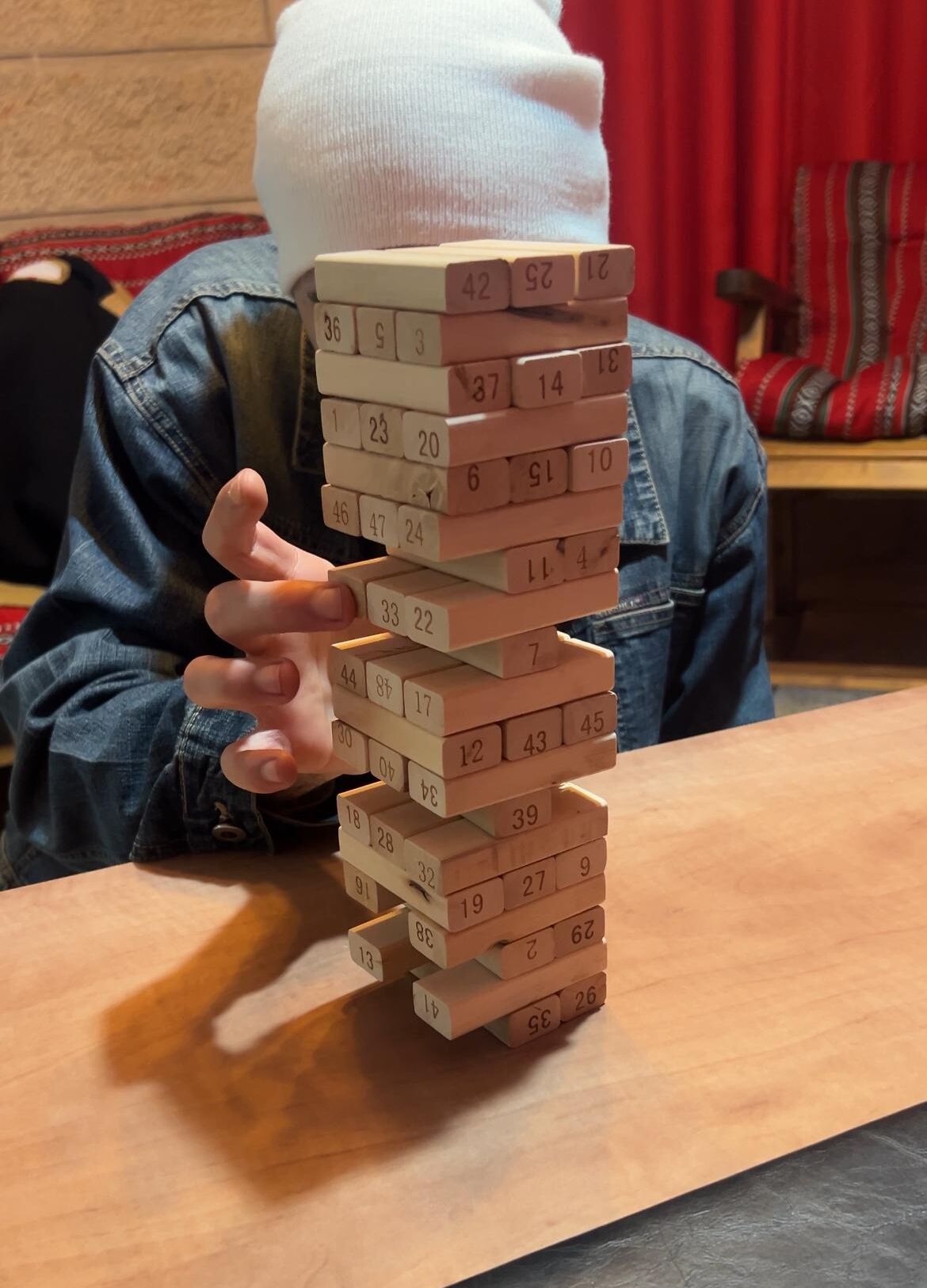 Une personne joue à un jeu de Jenga avec une tour en bois posée sur une table.