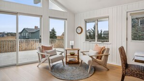 A spacious room with large windows, a round rug, two chairs, a small table with a bowl, and a clock on the wall. - Walk to Kennebunk beaches! 4BR home with marsh views, large deck, and firepit (Kennebunk)