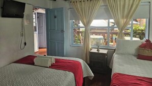 A room with two beds, a TV mounted on the wall, and a window with curtains. - One and a half blocks from the main square! Nice and cozy hotel. (Villa de Leyva)