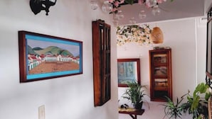 A hallway with a tiled floor, a framed painting, and hanging floral arrangements. - One and a half blocks from the main square! Nice and cozy hotel. (Villa de Leyva)
