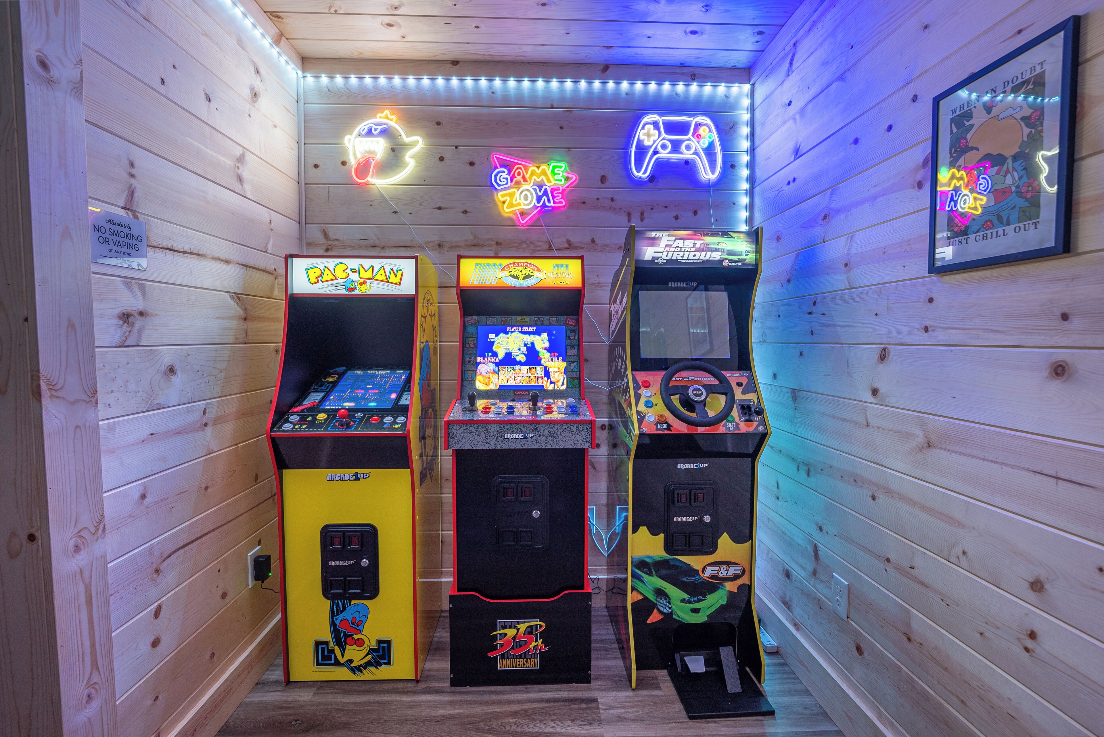 A row of arcade machines in a wooden-paneled room with neon signs and a framed poster on the wall.