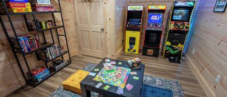 Una habitación con paredes de madera, una mesa con juegos de mesa, una máquina arcade de Pac-Man y un juego de Pac-Man en un estante.