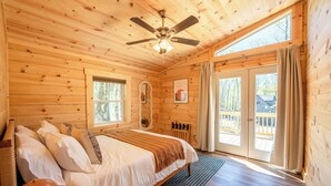 A wooden cabin bedroom with a bed, a ceiling fan, a window, and a view of the outside deck.
