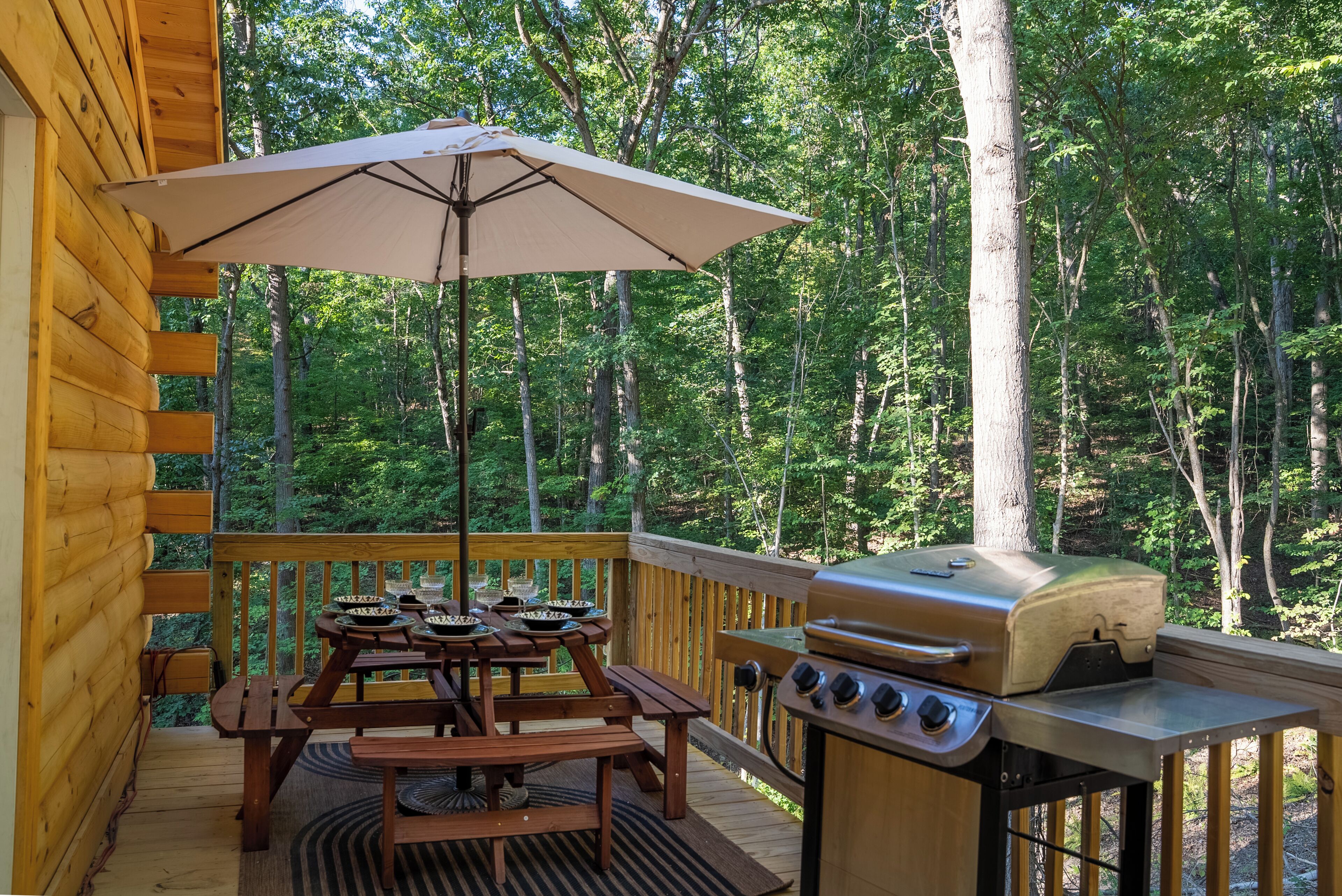 A wooden deck with a picnic table, grill, and umbrella.