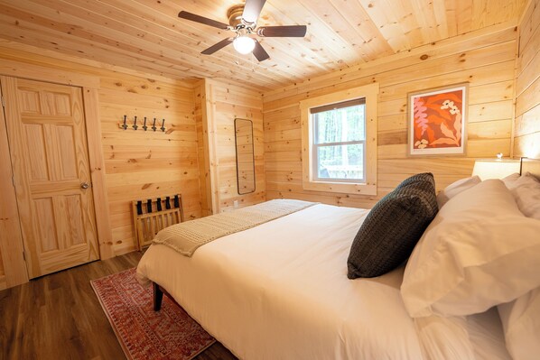 A wooden cabin bedroom with a bed, a ceiling fan, a window, and a door.