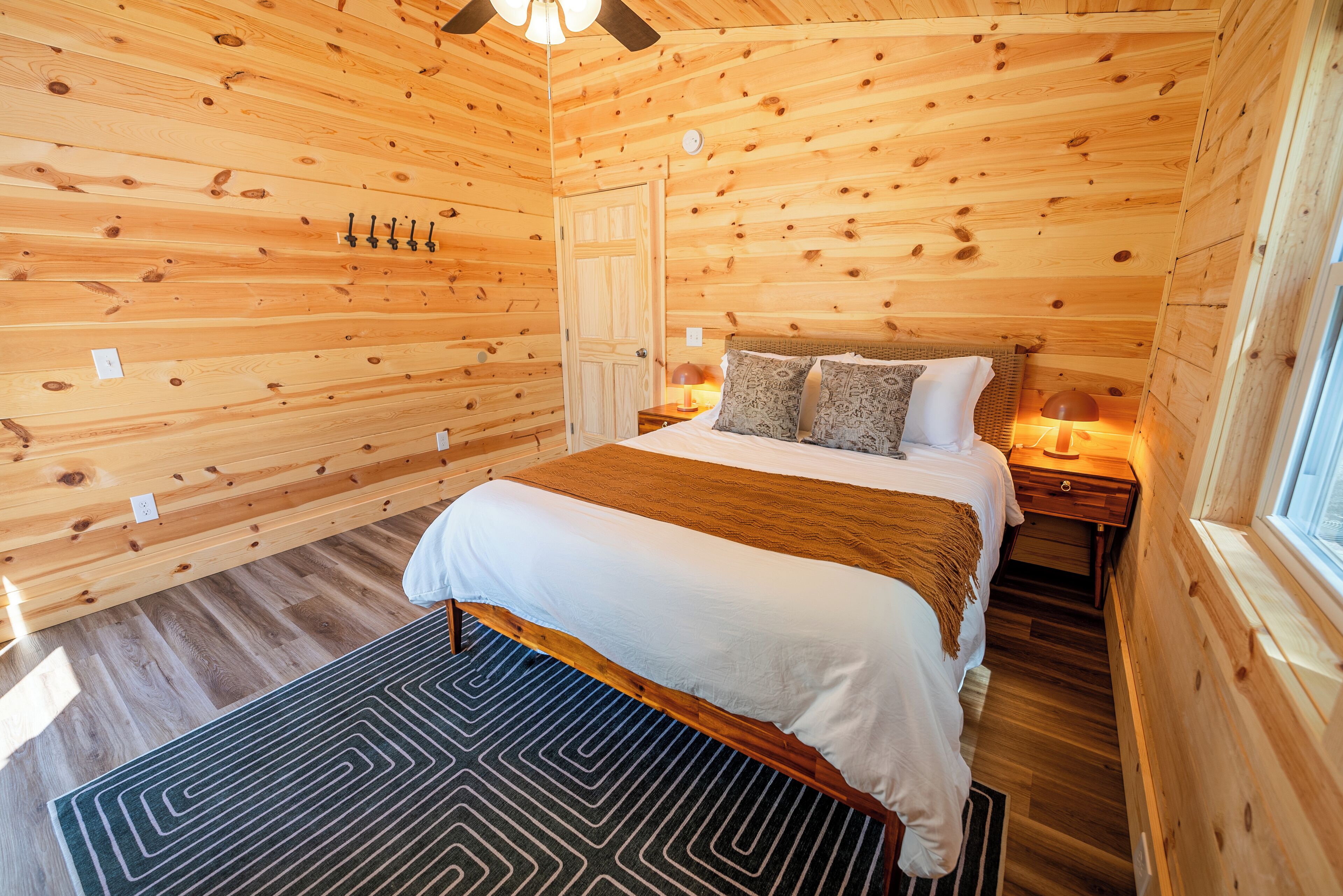 A wooden cabin bedroom with a bed, nightstands, and a window.