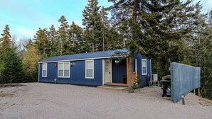 Une petite cabane d’un seul étage, à l’extérieur bleu, avec une porte d’entrée et un petit porche.