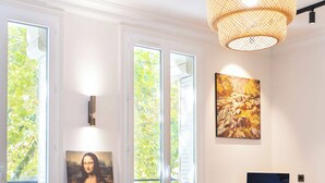 A modern living room with a large window, a painting, a computer desk, and a green sofa. - Résidence Reine - Paris -Boulogne (Boulogne-Billancourt)