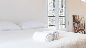Une chambre d’hôtel avec un lit, un tableau et une vue sur un bâtiment en pierre, visible par la fenêtre.
