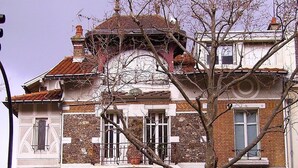Un bâtiment à deux étages, doté d’une façade en pierre, de fenêtres en arc de cercle et d’un toit recouvert de tuiles.
