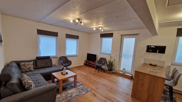 A modern living room with a sofa, armchairs, a coffee table, and a TV.