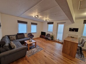 Ein modernes Wohnzimmer mit einer Couch, Sesseln, einem Couchtisch und einem Fernseher.