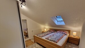 A bedroom with a skylight, a bed with patterned bedding, a bedside lamp, and a mirror.
