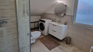 A modern bathroom with a glass shower enclosure, a washing machine, a toilet, and a sink with a mirror above.