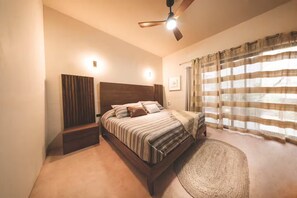 A bedroom with a bed, a ceiling fan, a nightstand, and a window with curtains.