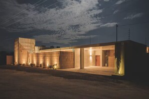 A modern building with a large entrance, a tall structure to the left, and a well-lit facade at night.
