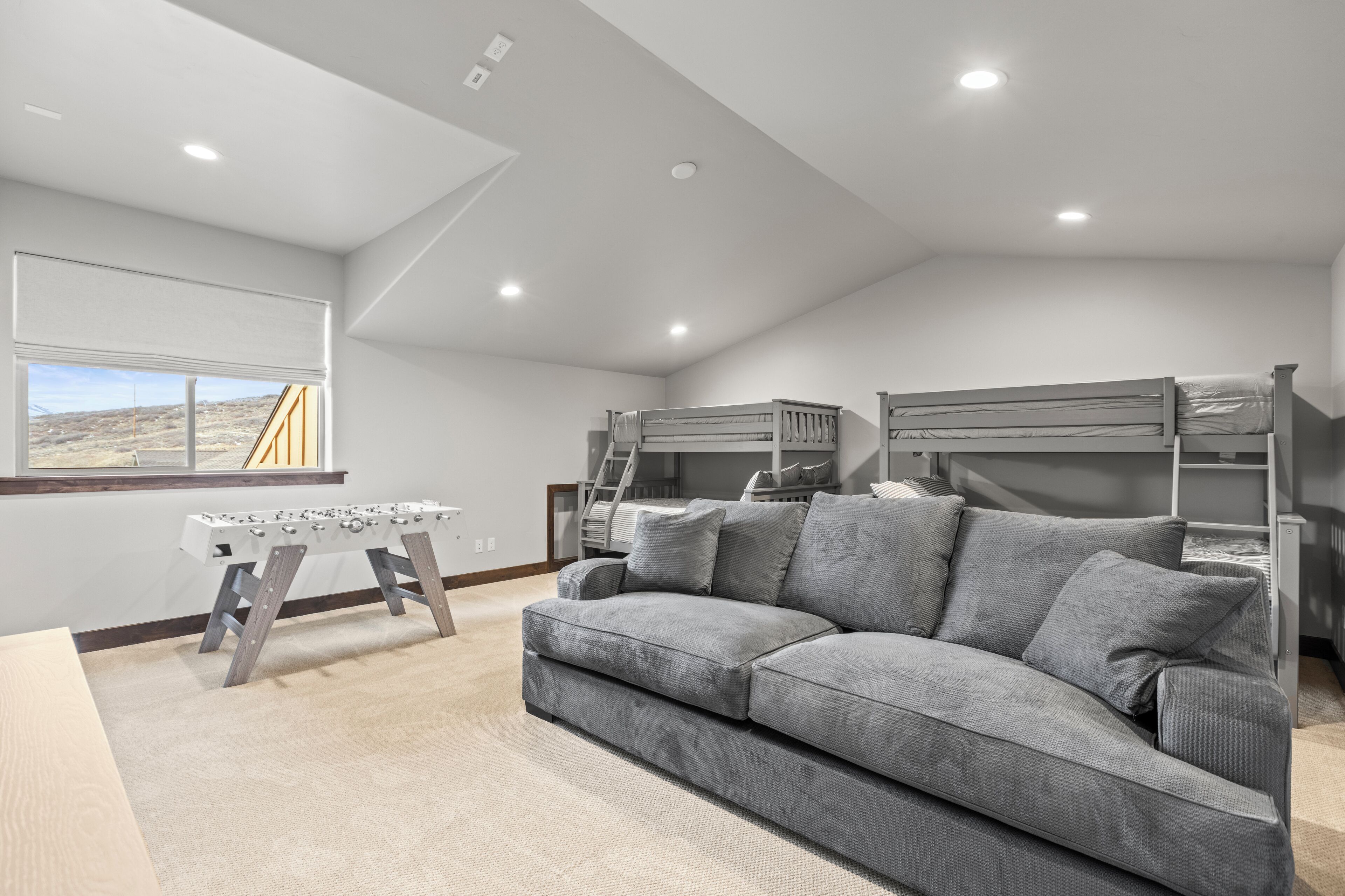 Una sala de estar moderna con un sofá gris, una mesa de fútbol de mesa y camas literas.