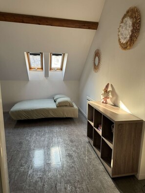 A small, loft-style bedroom with a sloped ceiling, two skylights, a bed, a wooden nightstand, and a wall-mounted shelf.