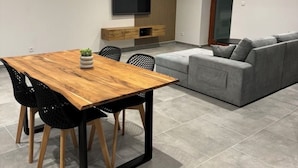 Un salon moderne avec une table à manger en bois, des chaises noires, un canapé gris et un téléviseur fixé au mur.