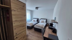 Une chambre avec deux lits, un bureau avec un ordinateur, une machine à café et une étagère avec une lampe et une bouteille.
