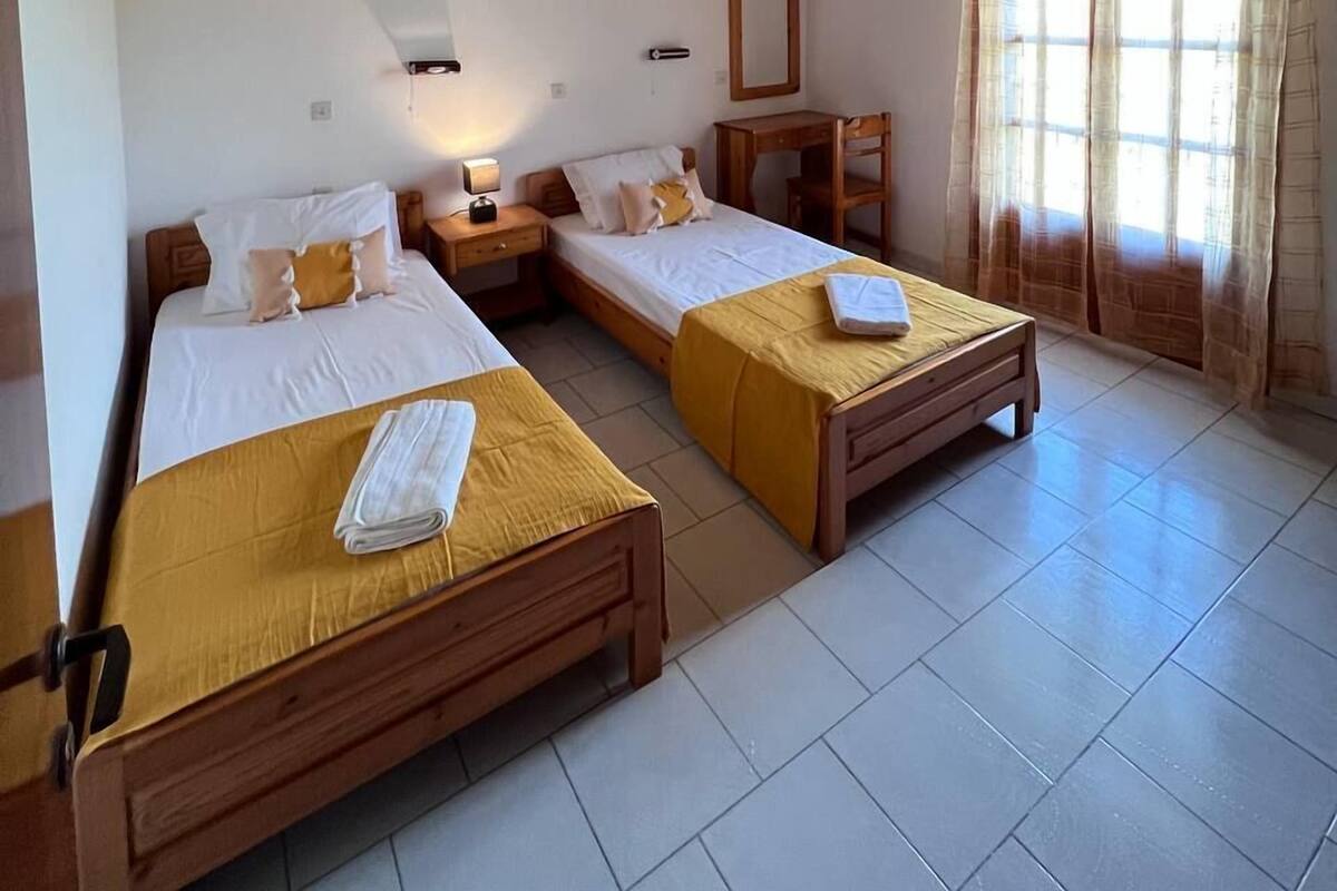 A room with two wooden beds, a nightstand, a bedside table, a mirror, and a window with curtains.